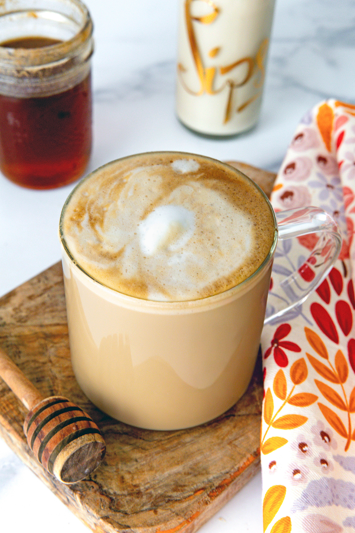 Overhead view of a Honey Almondmilk Flat White with honey syrup, honey stick, and almond milk in background.