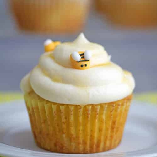 Closeup view of a honey bee cupcake with white frosting, honey drizzle, and bee icing decorations.