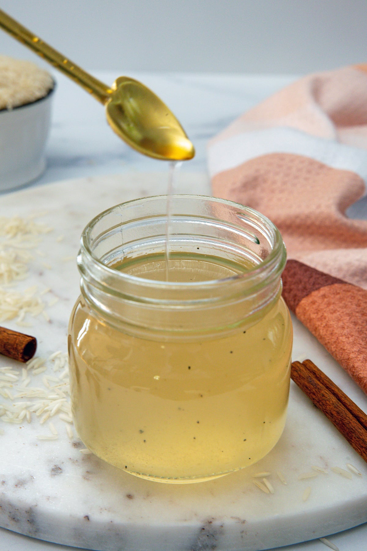 Small mason jar of horchata syrup with syrup dripping off heart-shaped spoon.