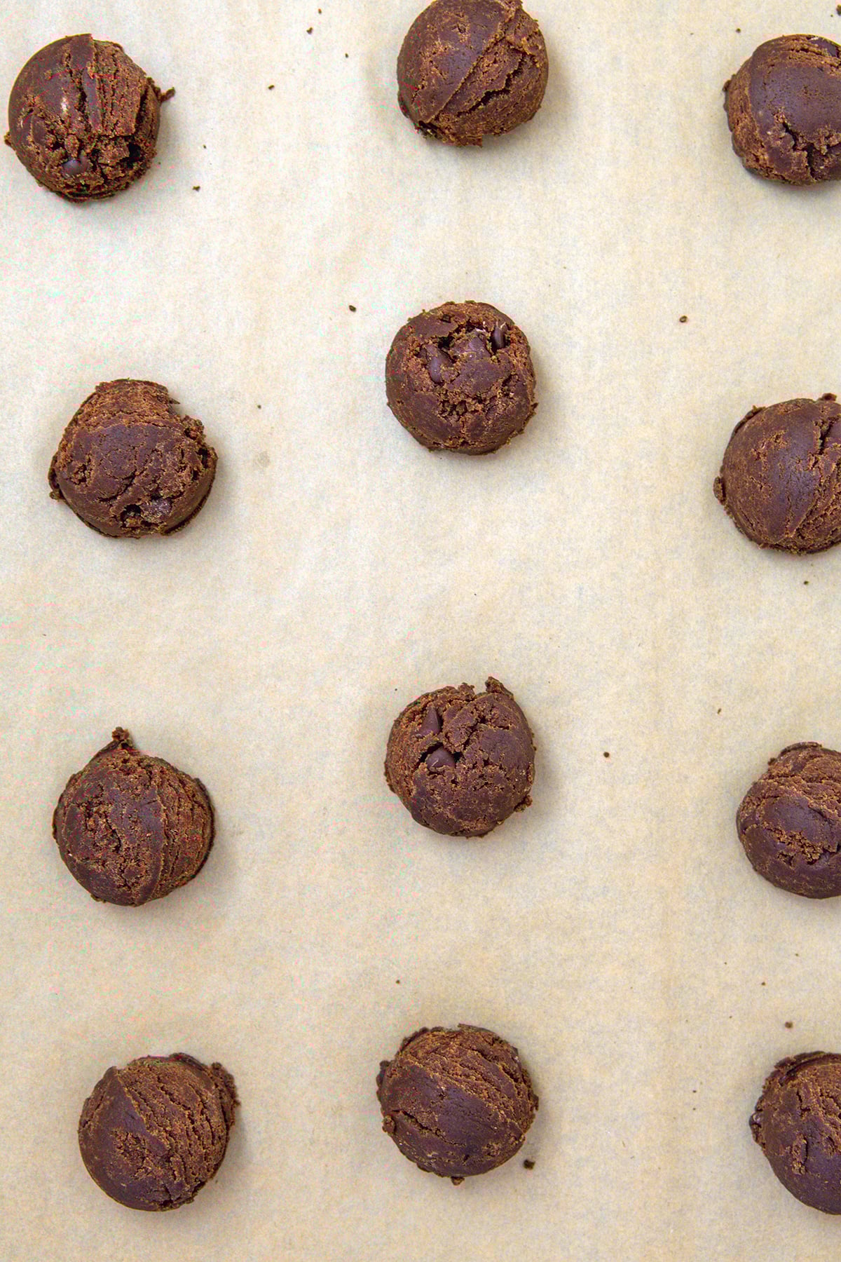 Chocolate cookie dough balls on a parchment paper lined baking sheet.