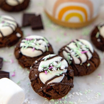 Closeup view hot chocolate cookies with marshmallow middle, chocolate drizzle, and sprinkles.