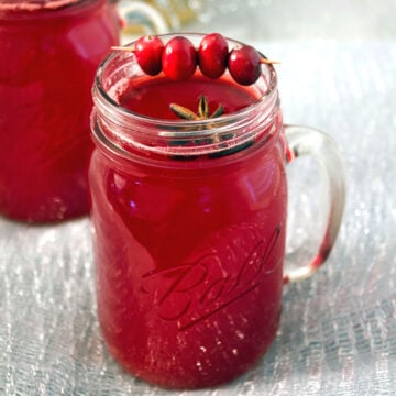 Closeup view of a hot spiced cranberry cocktail in a mason jar with cranberry and star anise garnish.