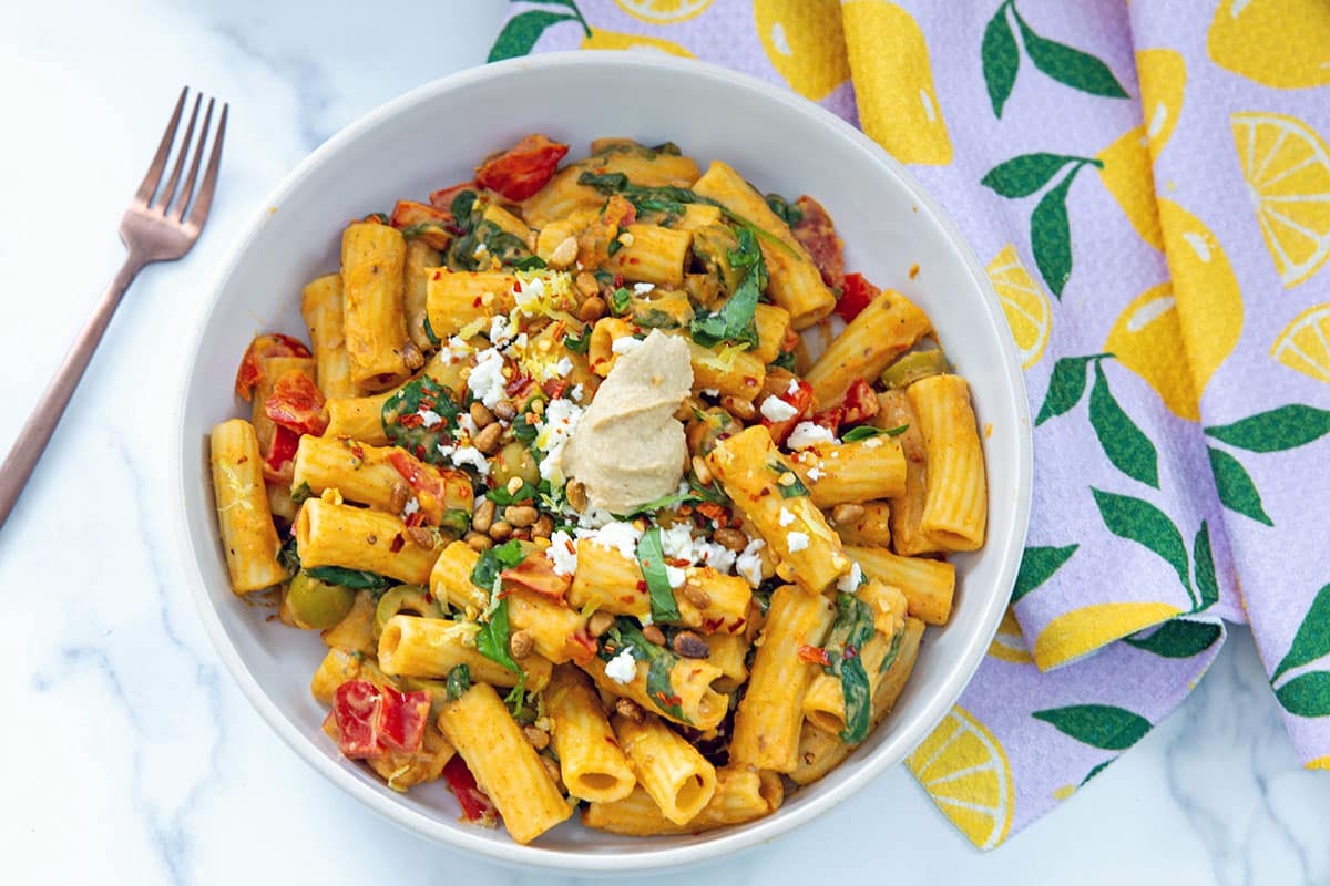Landscape overhead view of a bowl of hummus pasta with scoop of hummus on top and fork on the side.