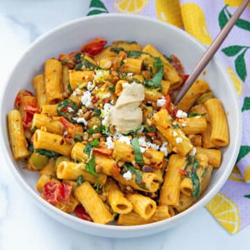Closeup view of hummus pasta with tomatoes, peppers, spinach, basil, and dollop of hummus.