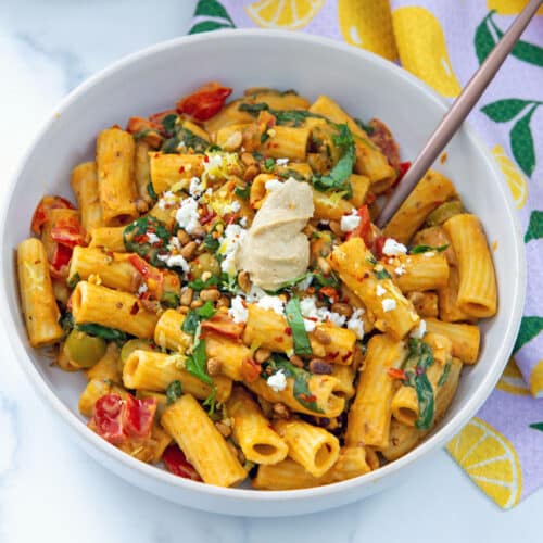 Closeup view of hummus pasta with tomatoes, peppers, spinach, basil, and dollop of hummus.