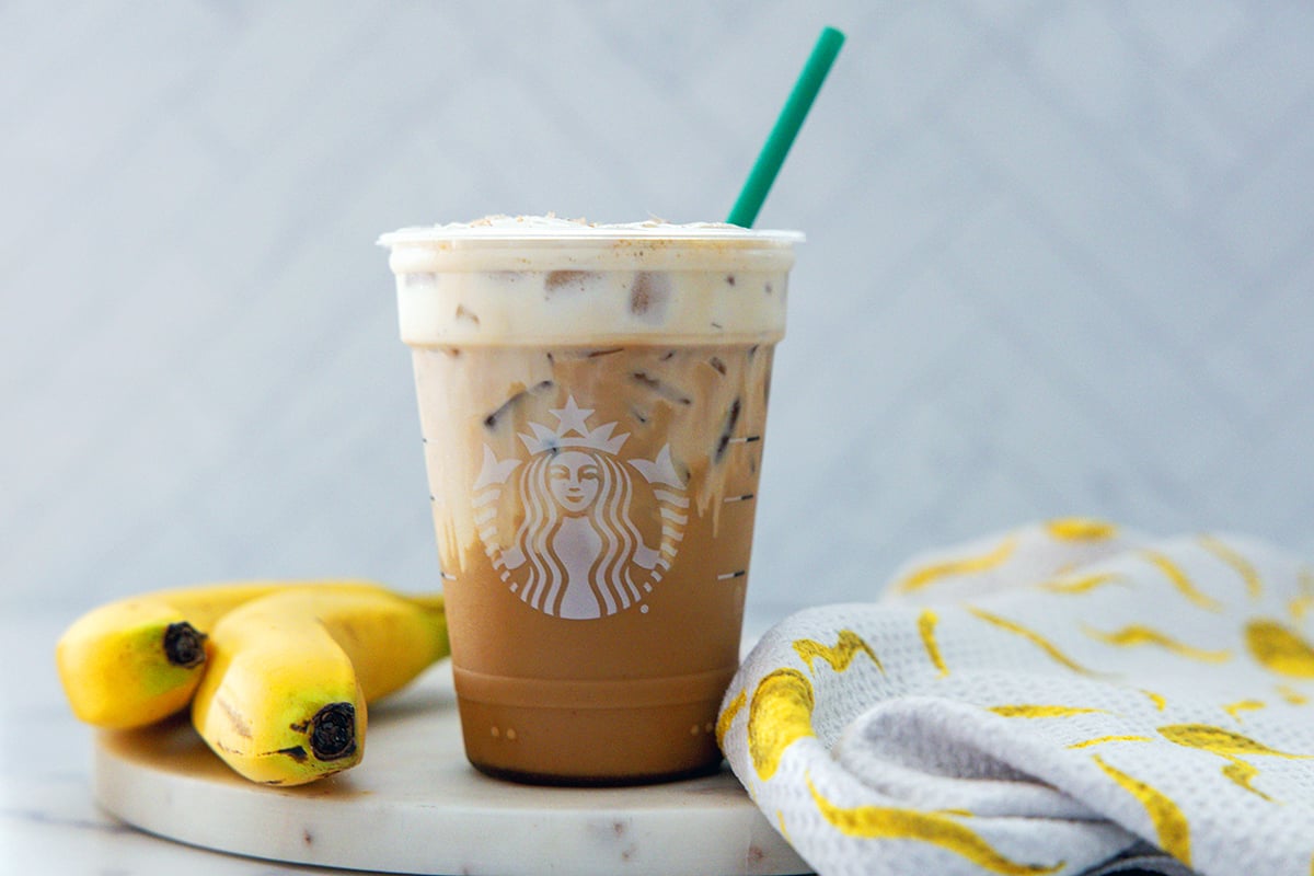 Landscape head-on view of an Iced Banana Bread Latte in a Starbucks cup with green straw.