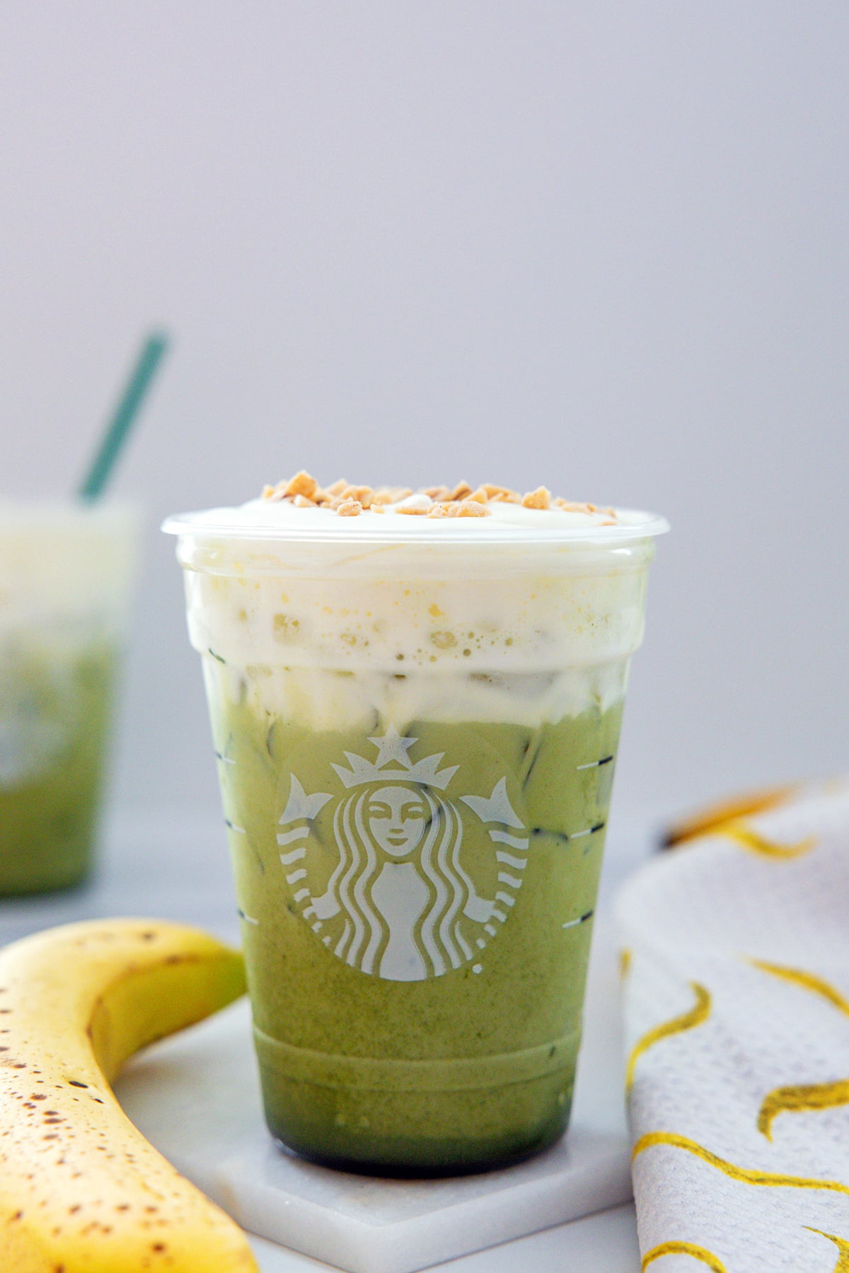 Banana bread matcha topped with cold foam in a Starbucks cup with banana next to it.