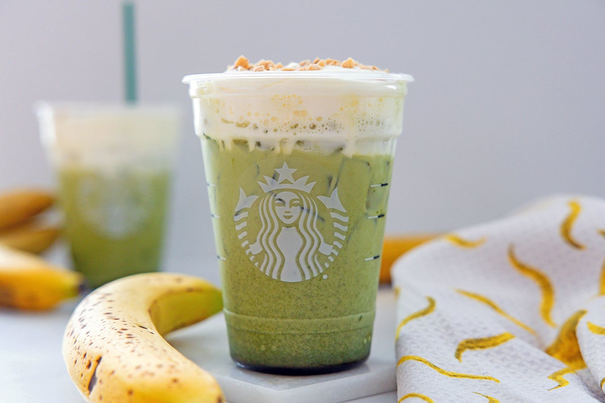 Landscape head-on view of an Iced Banana Bread Matcha with second drink in background and bananas all around.