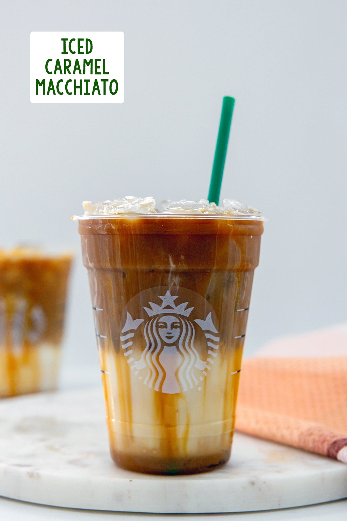 Head-on view of an Iced Caramel Macchiato in a Starbucks cup with green straw and recipe title at top.