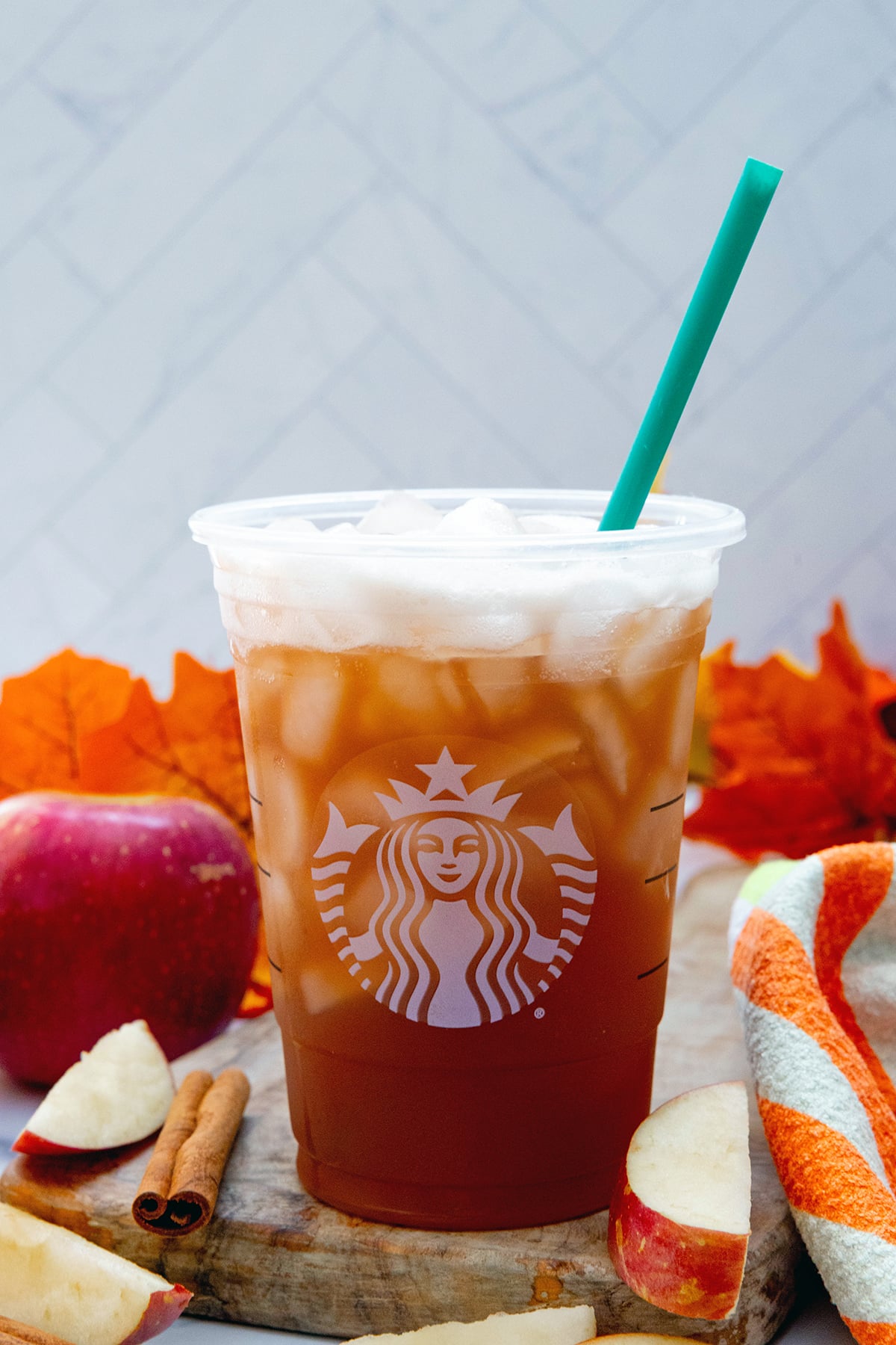 Head-on view of an Iced Chaider in a Starbucks cup with leaves and apples in background.