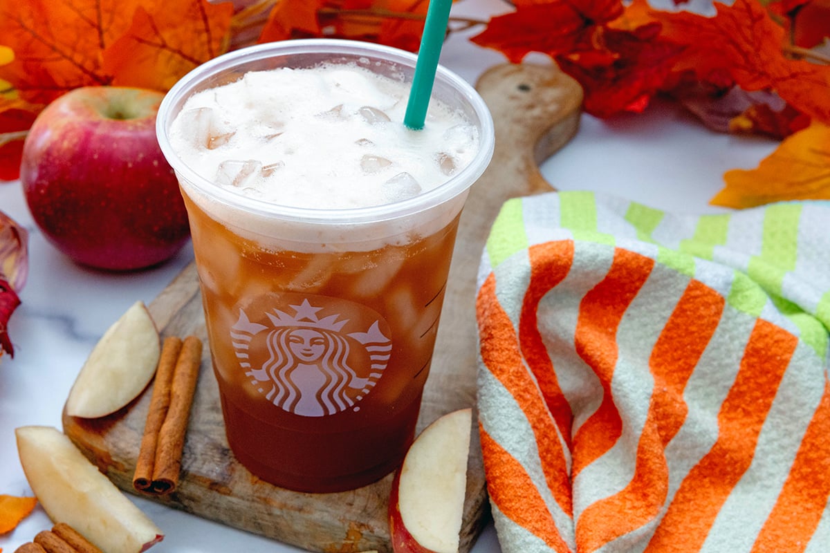 Landscape overhead view of an iced Chai with green straw with apples all around.