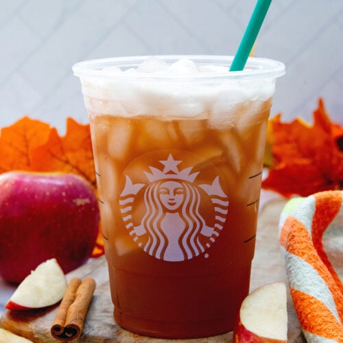 Close-up view of an Iced Chaider with apples and cinnamon sticks all around.