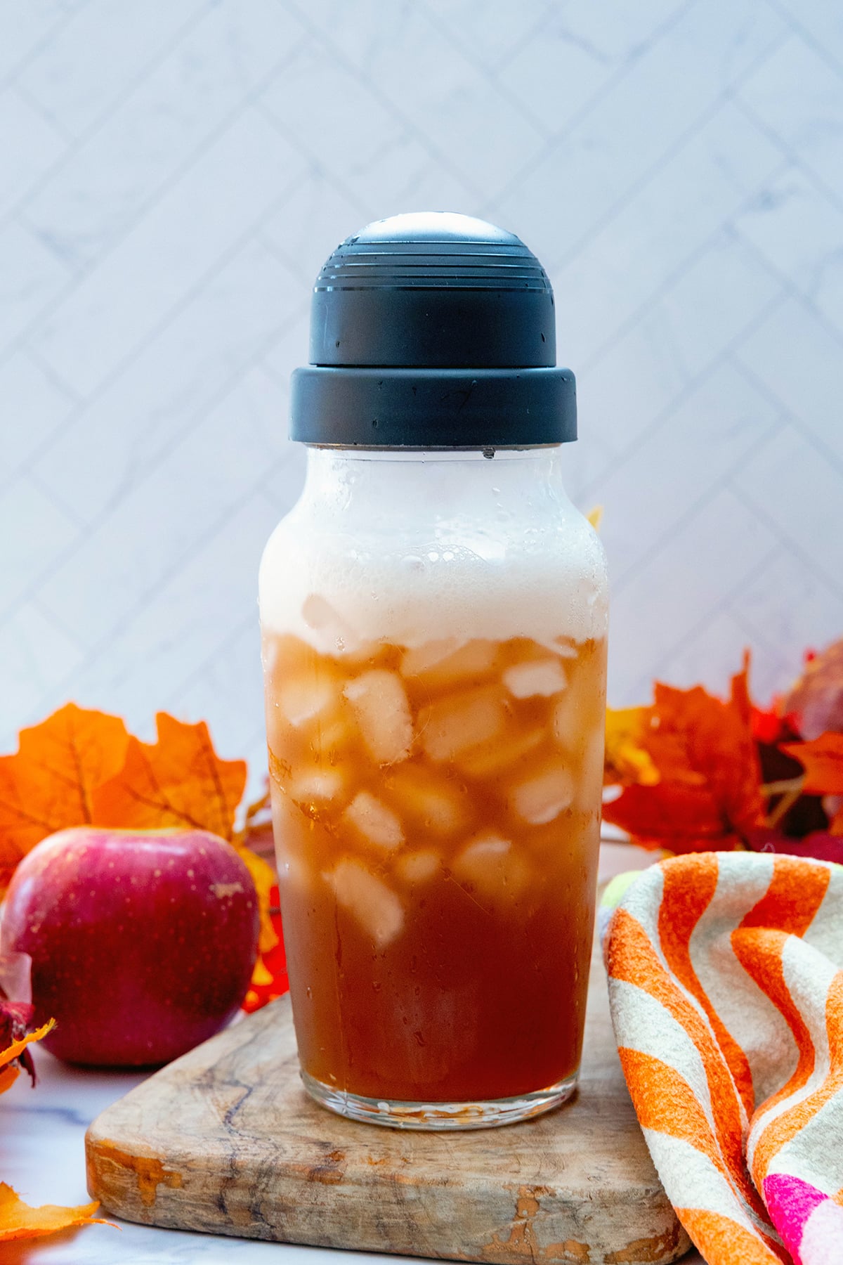 Head-on view of an Iced Chaider in a shaker bottle with leaves and apple in background.