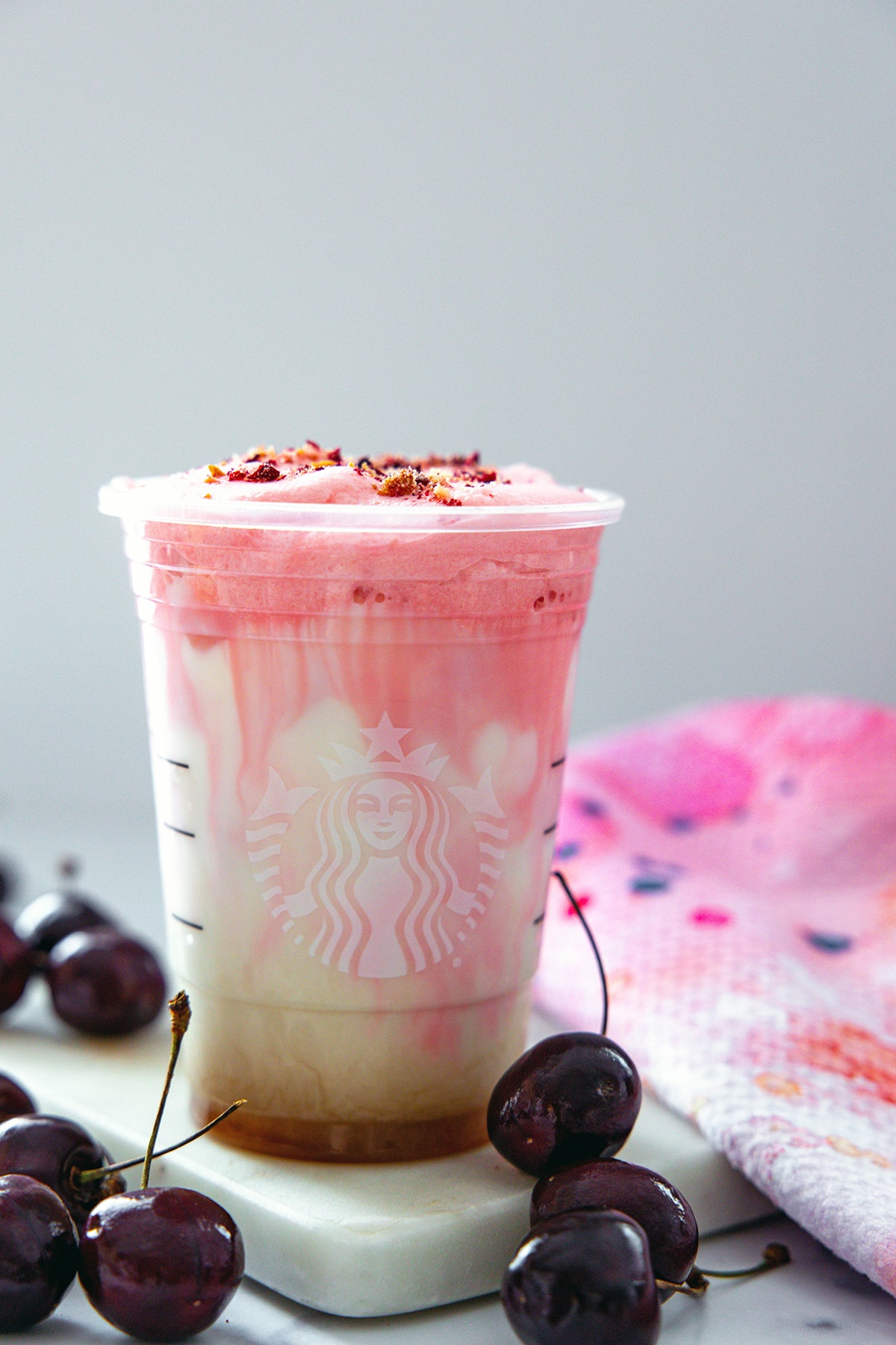 Head-on view of an iced cherry chai latte in cup with fresh cherries all around and cherry/cookie mix on top of foam.