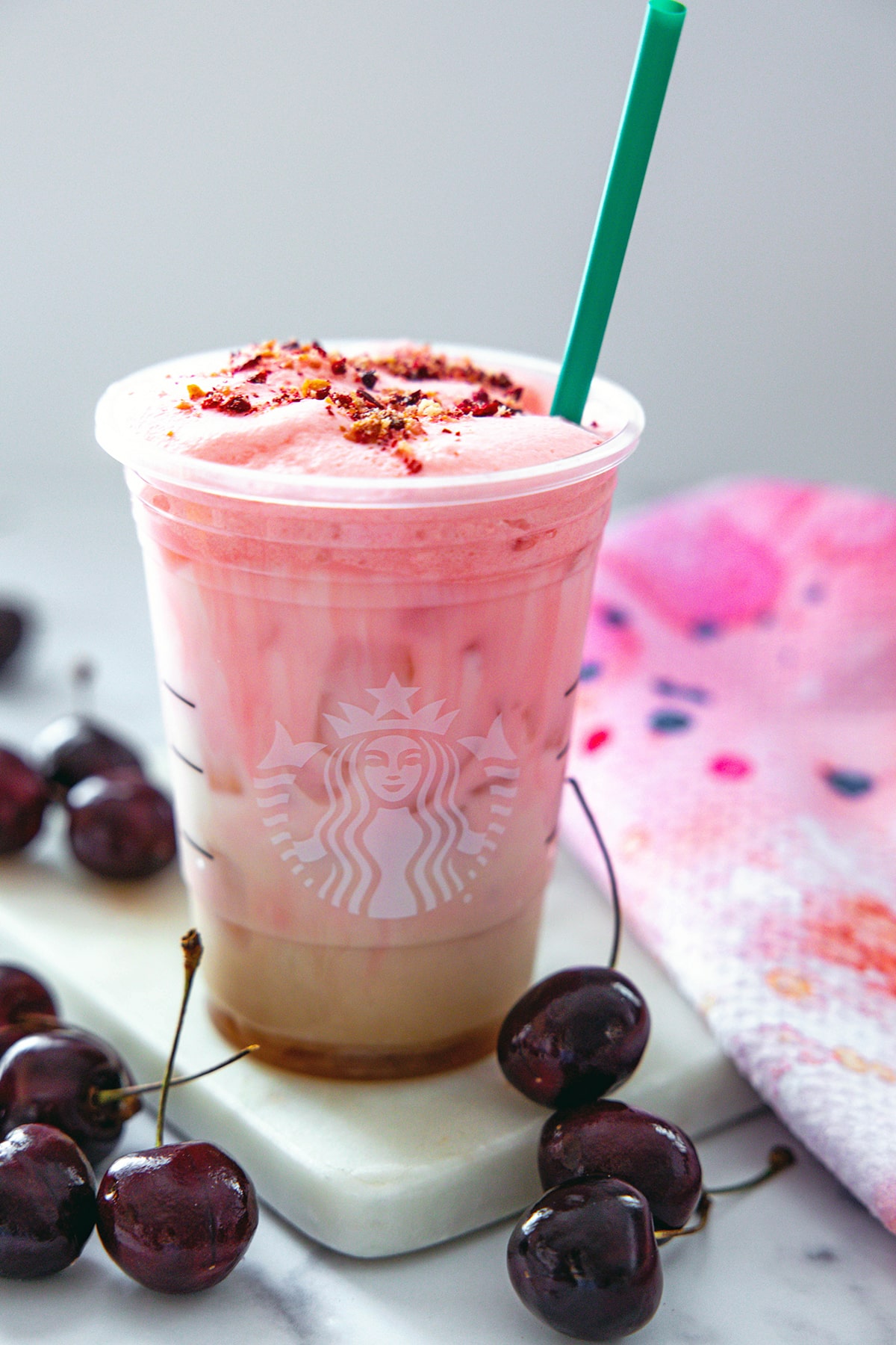 Overhead view of Iced Cherry Chai latte with green straw, showing freeze-dried cherry and vanilla cookie crumble on top.
