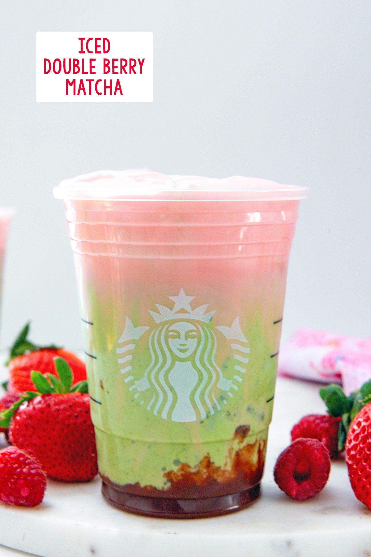 Head-on view of an Ice Double Berry Matcha in a Starbucks cup with strawberry puree on bottom, matcha and milk middle, and raspberry cold foam topping with recipe title at top of photo.