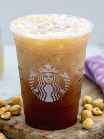 Closeup of iced hazelnut oatmilk shaken espresso in Starbucks cup with hazelnuts all around.