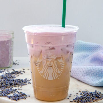 Closeup view of an Iced Lavender Cream Chai in a Starbucks cup with a green straw.