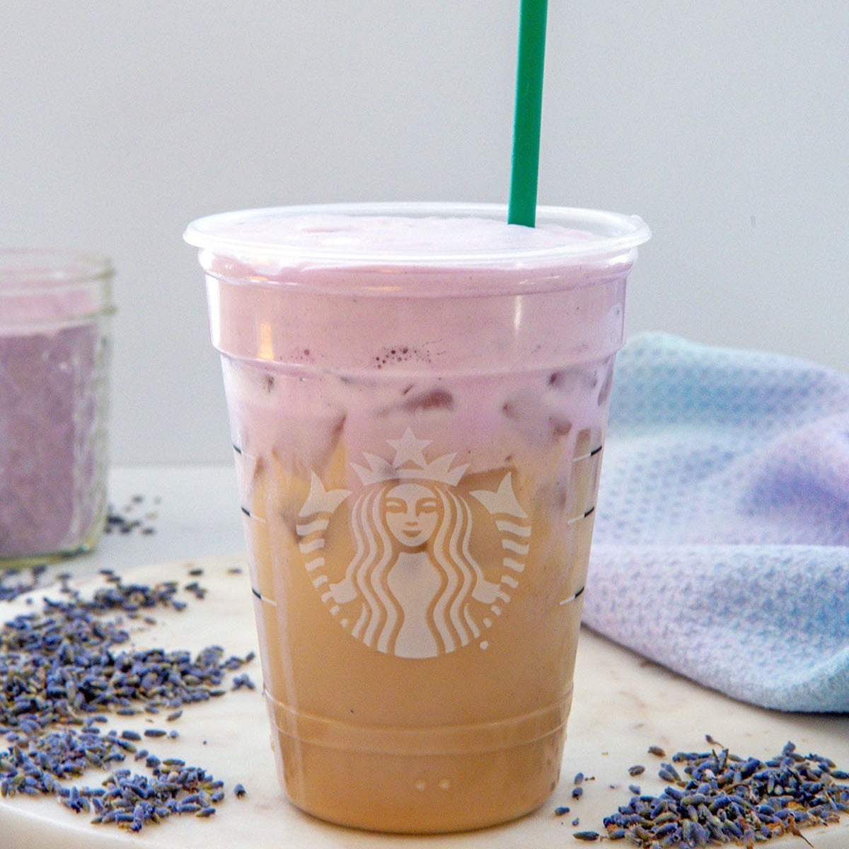Closeup view of an Iced Lavender Cream Chai in a Starbucks cup with a green straw.