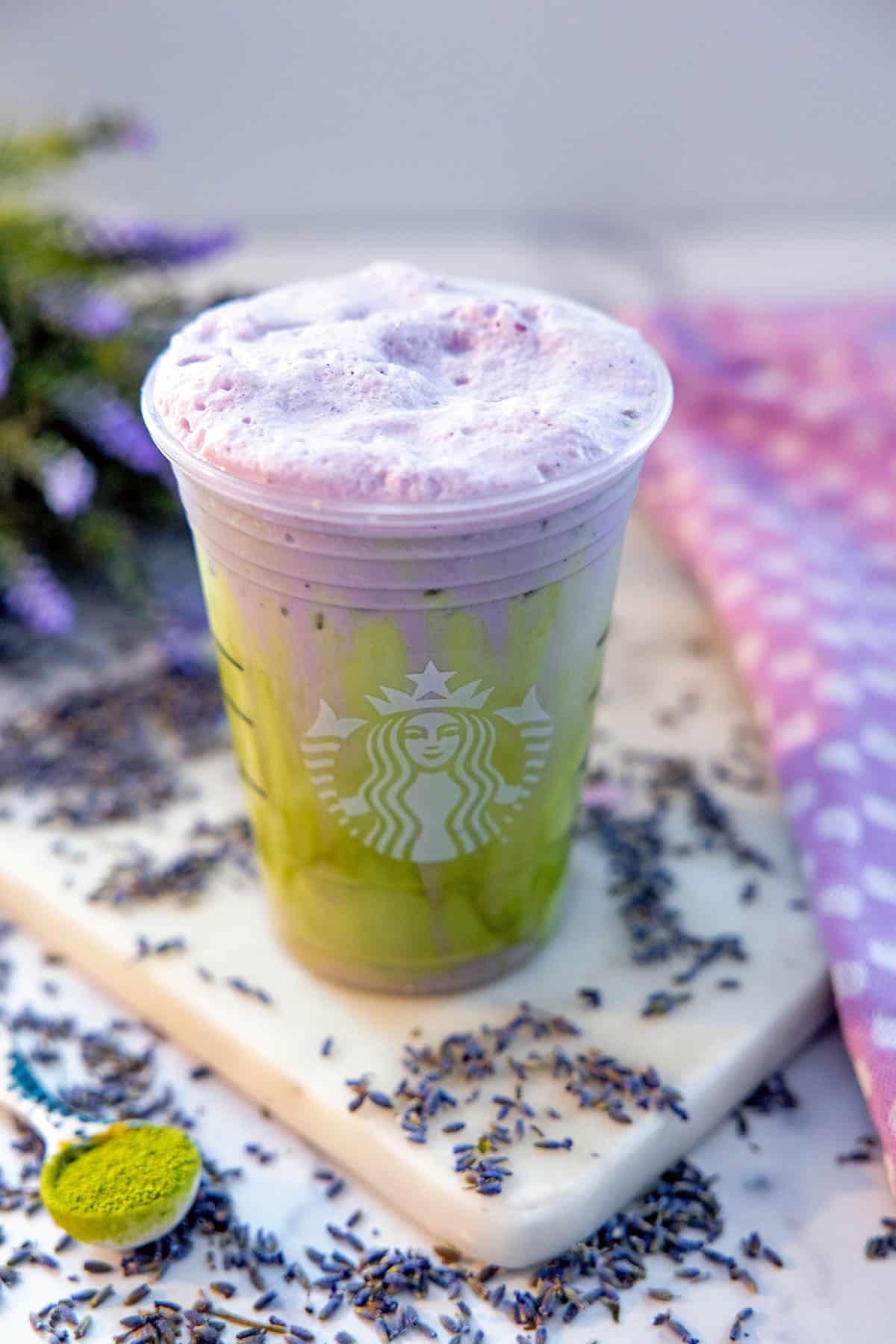 Overhead view of an iced matcha with lavender cold foam with lavender flowers all around and a spoonful of matcha.