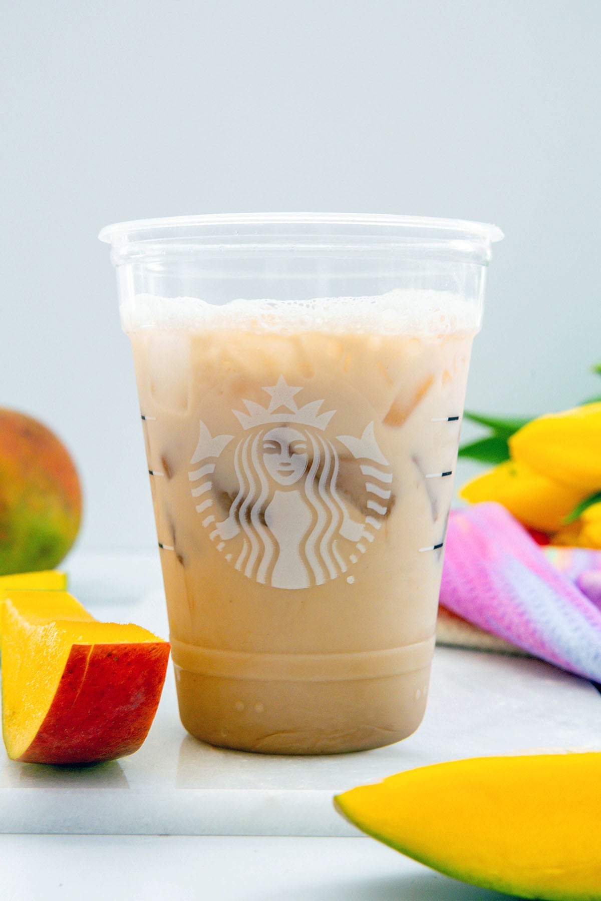 Head-on view of chai concentrate and milk in a Starbucks cup with sliced mango on the side.