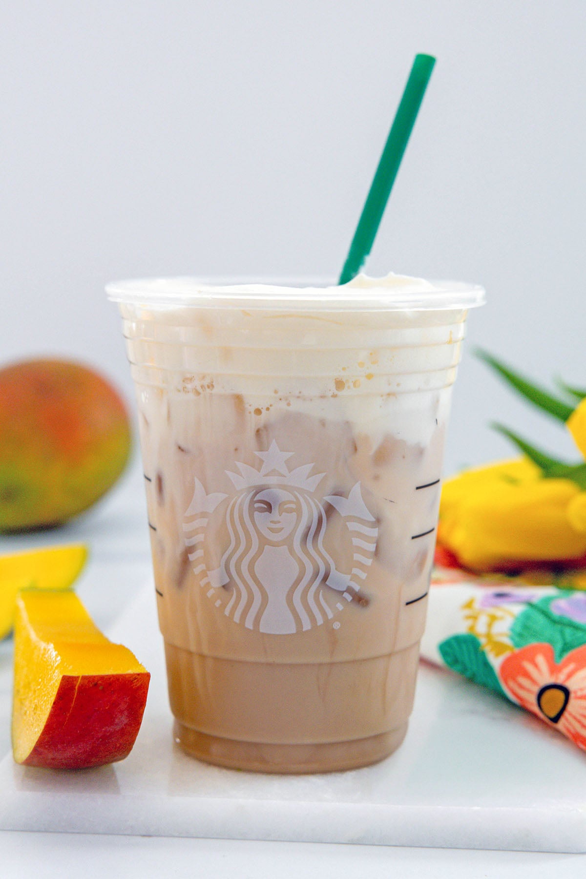 Head-on view of an Iced Mango Cream Chai with a green straw and sliced mango all around.
