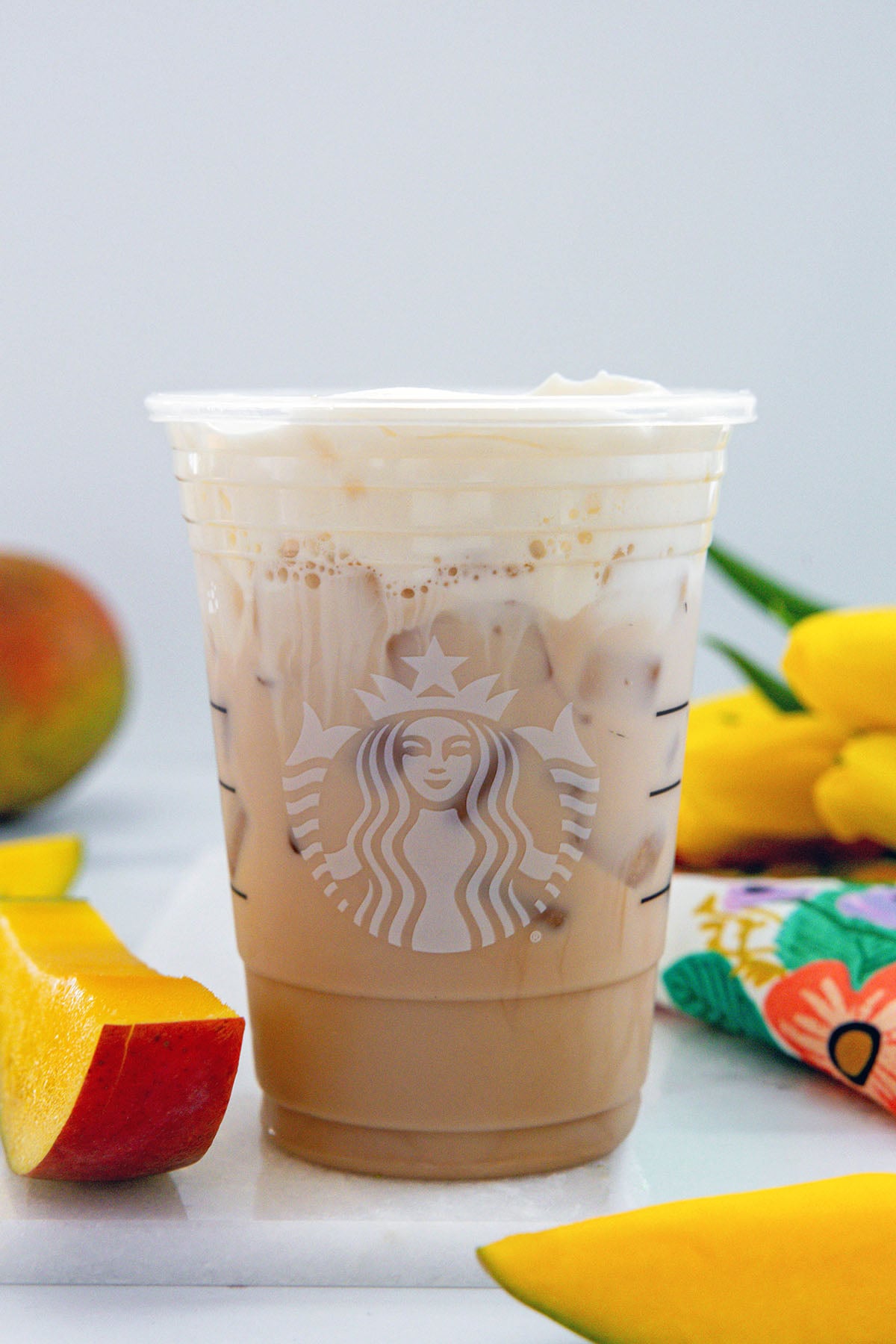Head-on view of an Iced Mango Cream Chai in a Starbucks cup with sliced mango all around.