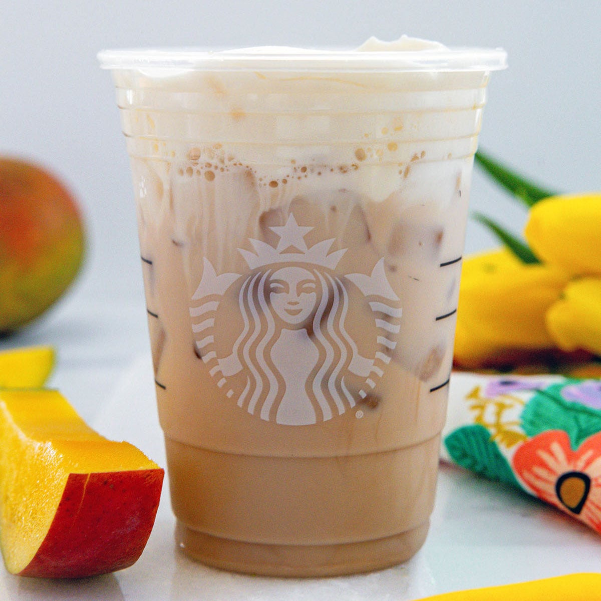 Closeup view of a Starbucks Iced Mango Cream Chai with sliced mango next to cup.