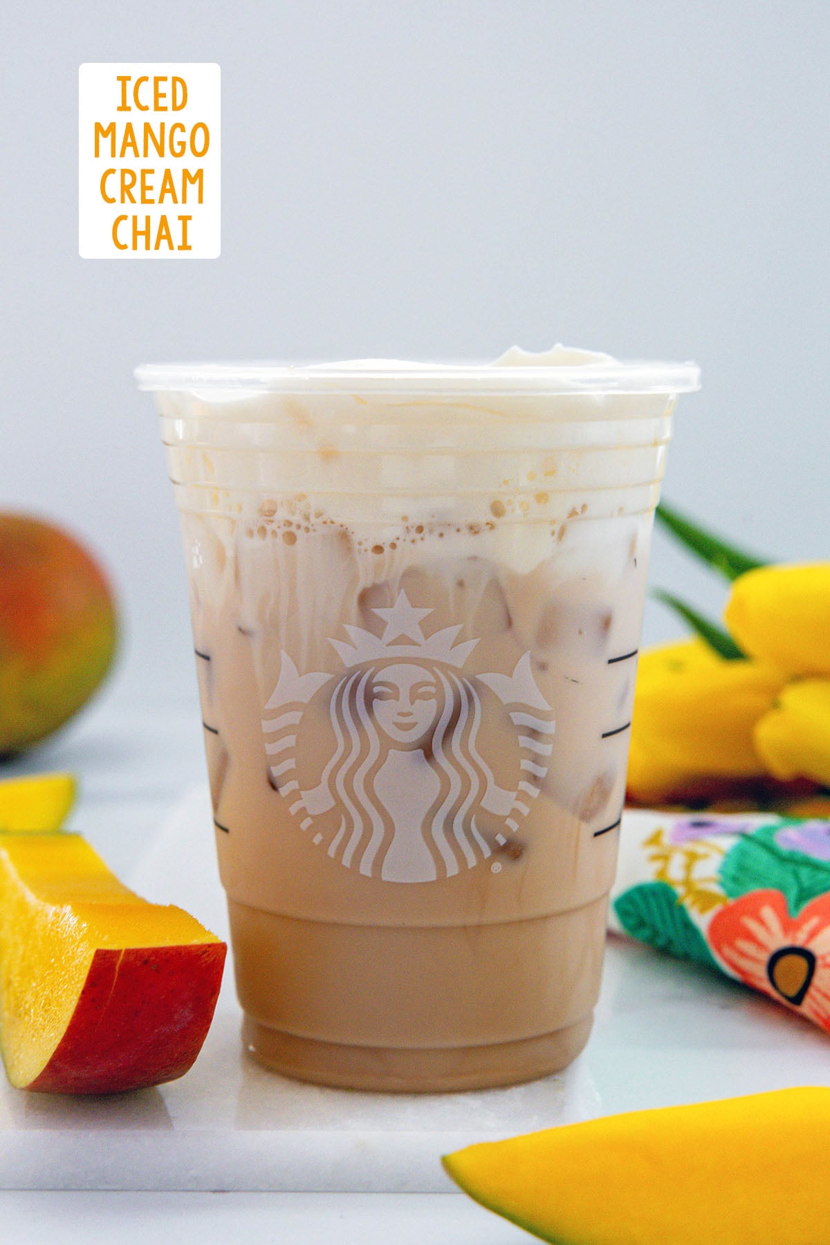 Head-on view of an Iced Mango Cream Chai in a Starbucks cup with sliced mango all around and recipe title at top.