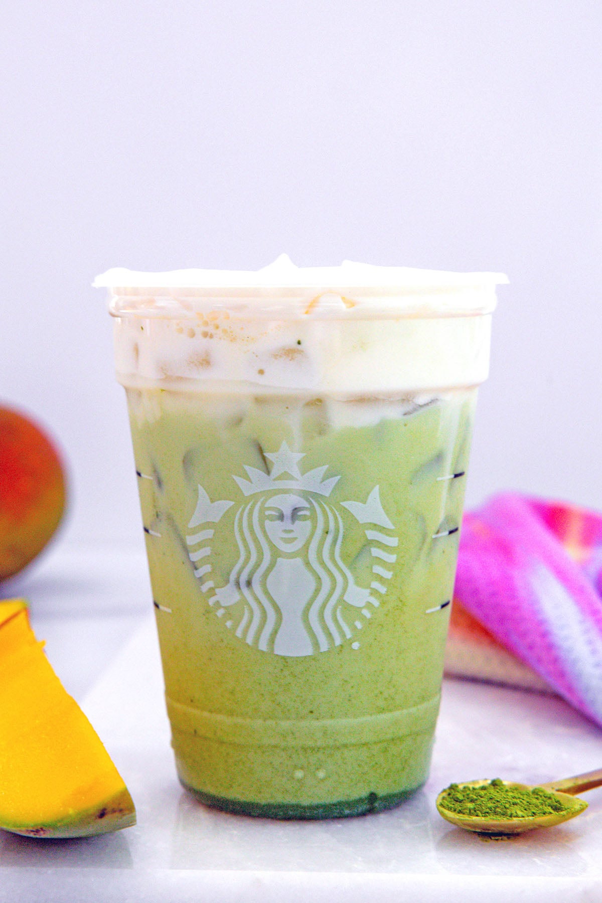 Head-on view of an Iced Mango Cream Matcha with cold foam on top and sliced mango in background.