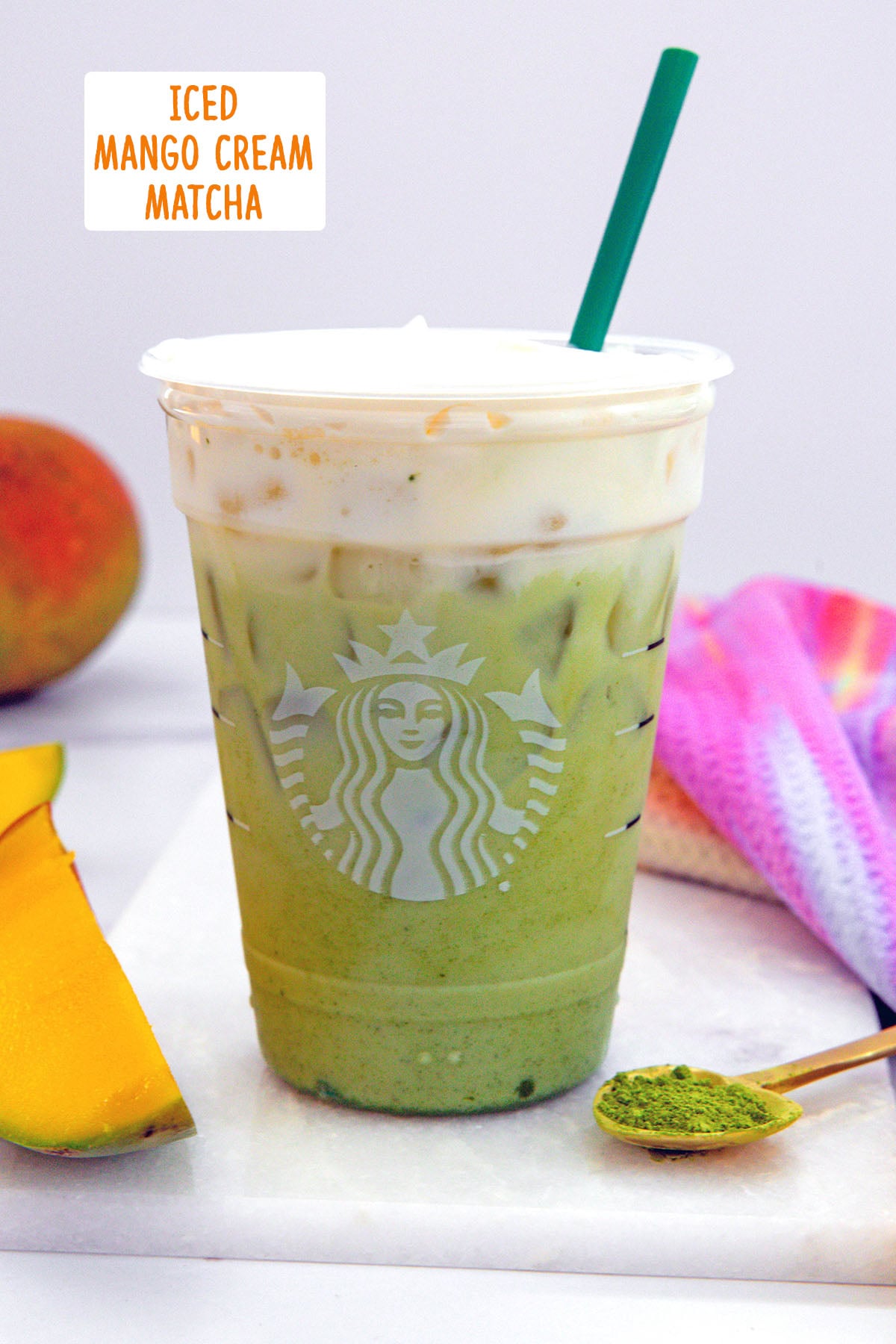Head-on view of an Iced Mango Cream Matcha with sliced mango and matcha powder in background with recipe title at top.