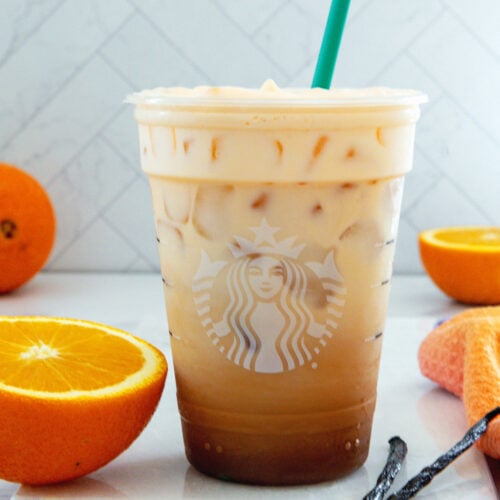 Closeup view of an Iced Orange Cream Latte in a Starbucks cup with green straw.