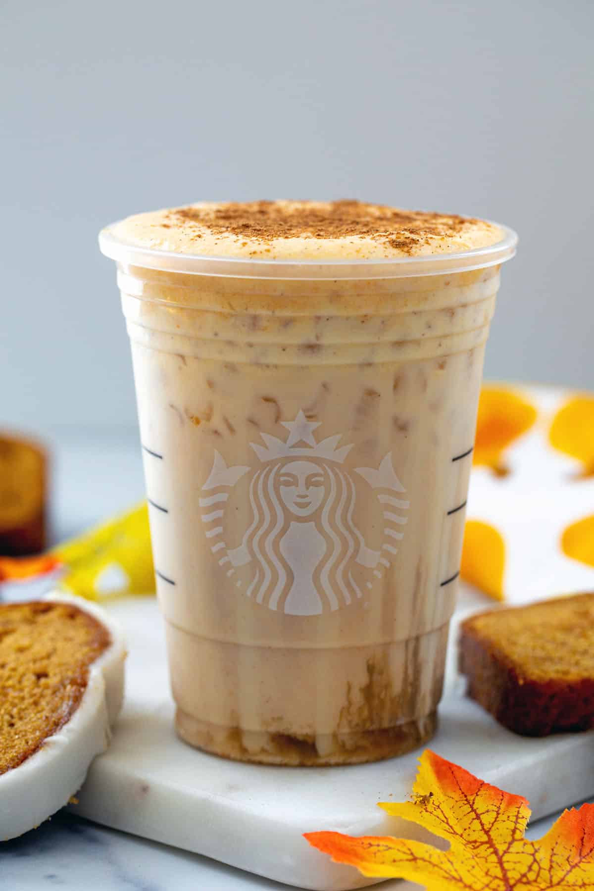 Head-on view of a Starbucks cup filled with an Iced Pumpkin Cream Chai Tea Latte with pumpkin bread around.