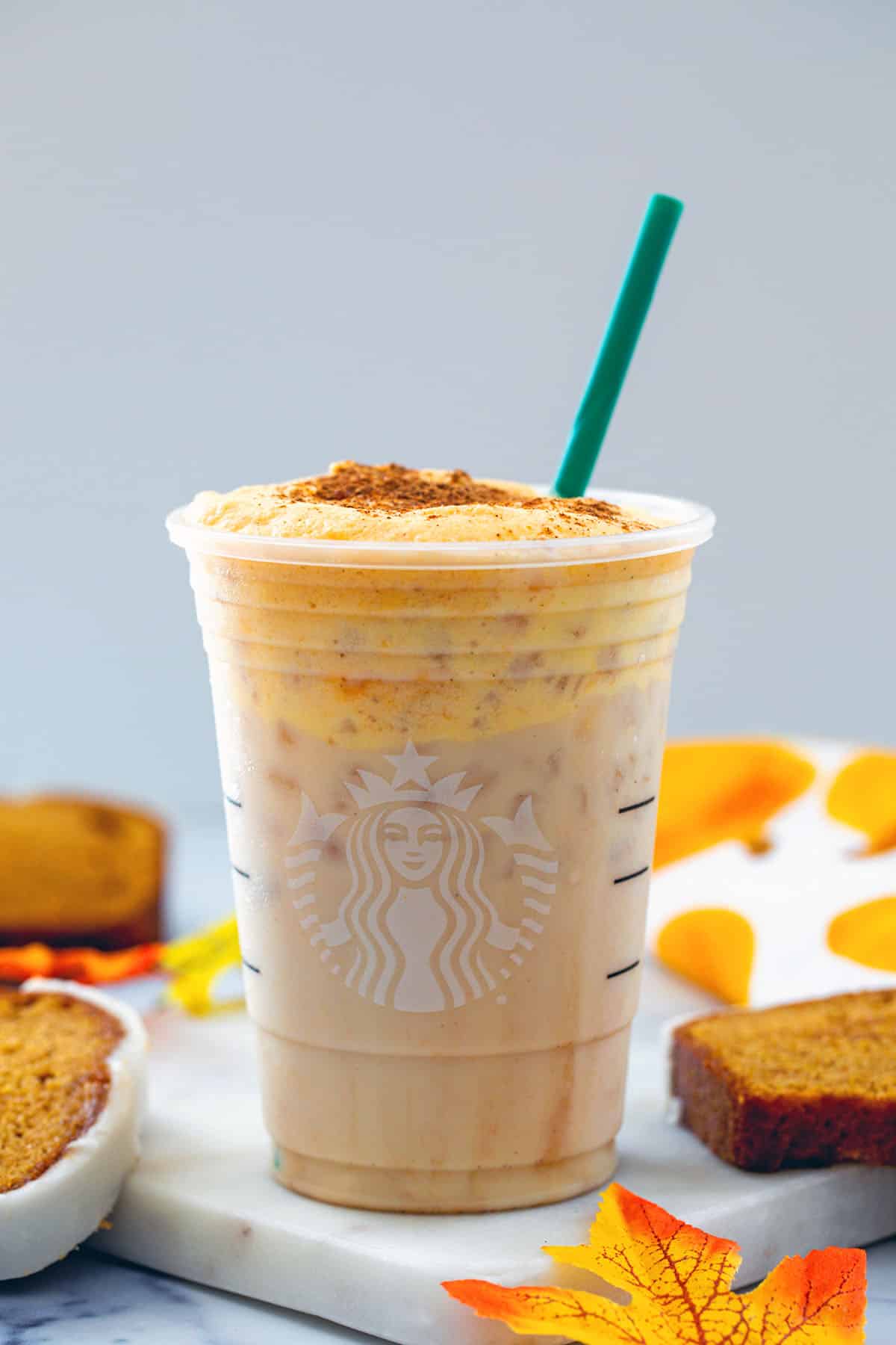 Head-on view of iced pumpkin cream chai tea latte with green straw with pumpkin bread all around.