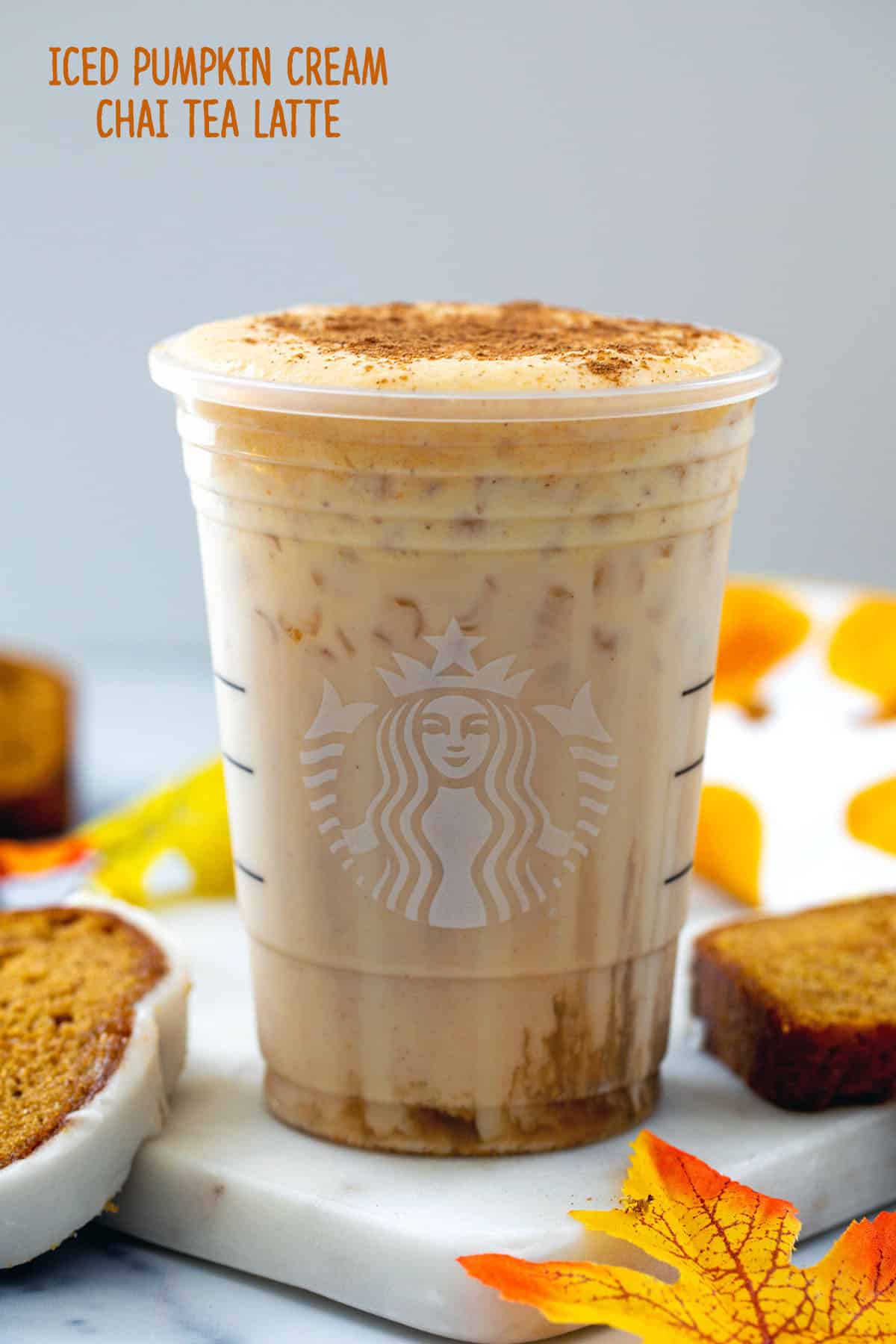 Head-on view of a Starbucks cup filled with an Iced Pumpkin Cream Chai Tea Latte with pumpkin bread around and recipe title at top.