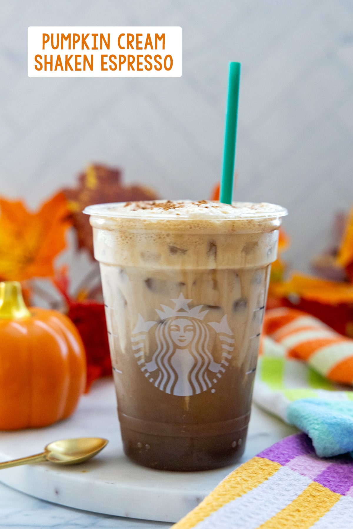 Head-on view of an Iced Pumpkin Cream Shaken Espresso in a Starbucks cup with green straw with recipe title at top of photo.