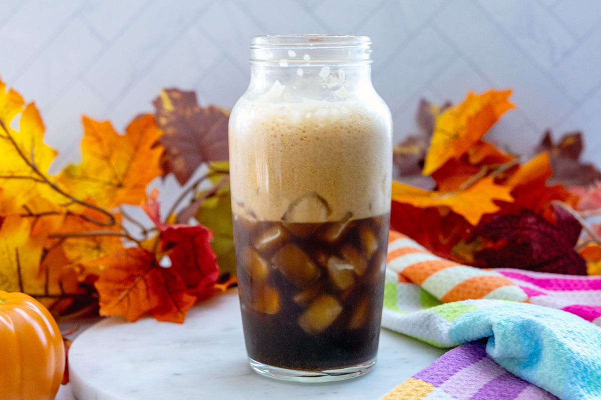Landscape head-on view of clear shaker filled with espresso and ice with froth.