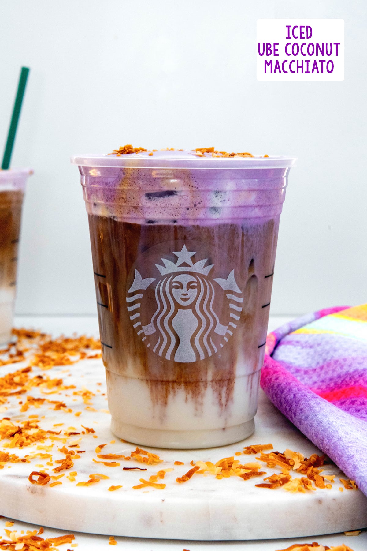 Head-on view of an Iced Ube Macchiato wit layer of milk, layer of espresso, and layer of ube coconut cold foam with recipe at top of photo.