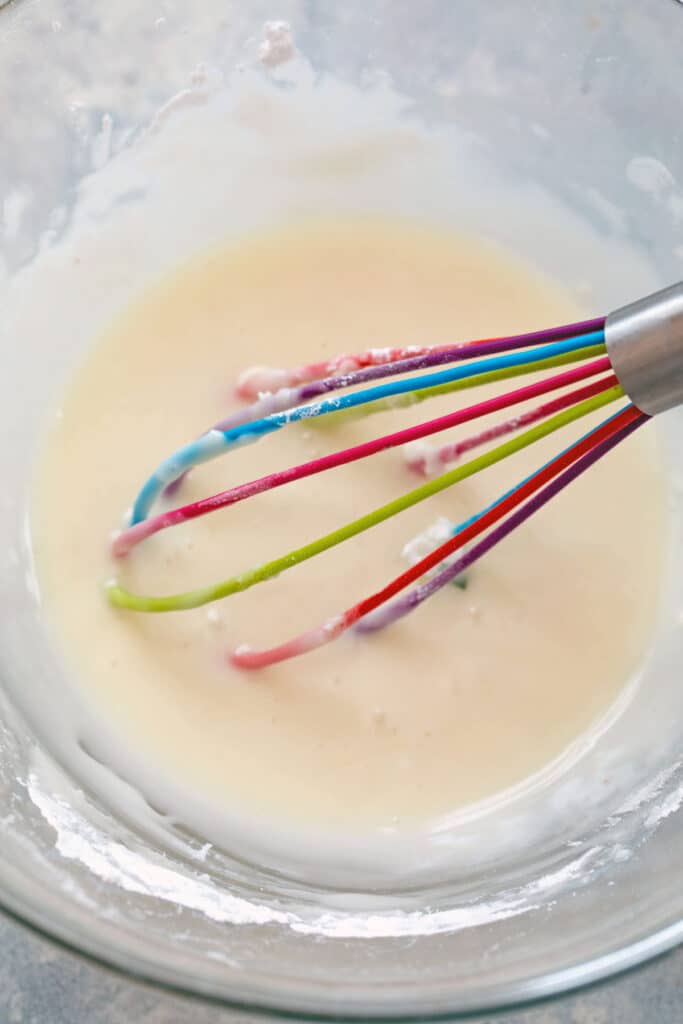 Vanilla icing in bowl with rainbow whisk.