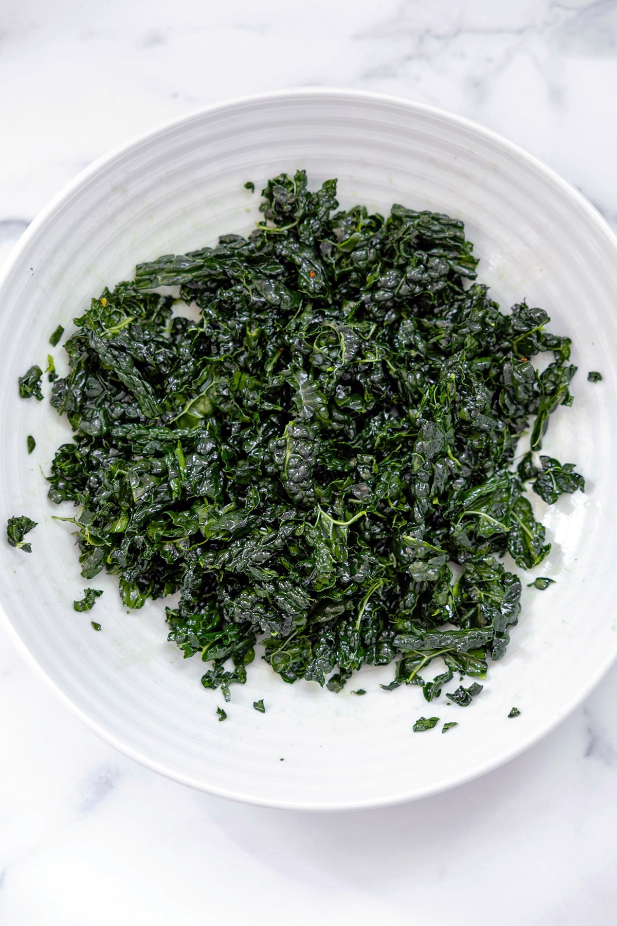 Roughly chopped kale massaged with olive oil and lemon juice in bowl.