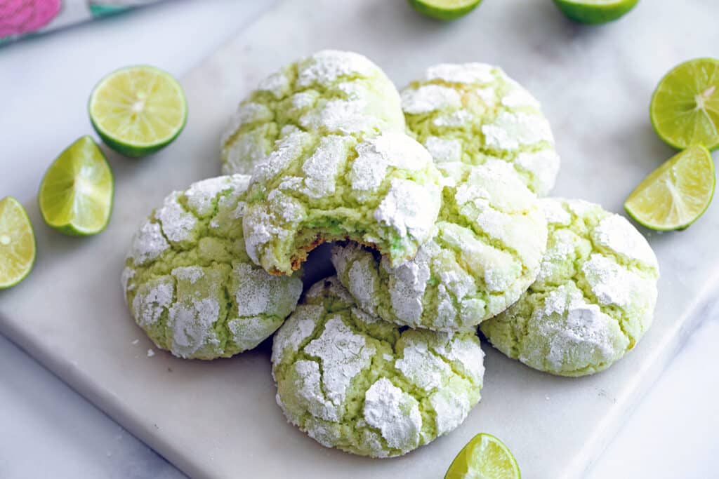 Landscape overhead view of multiple key lime cookies, one with a bite taken out of it, with key lime wedges all around.