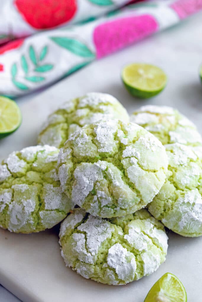 Green key lime cookies on a marble platter with key limes all around.