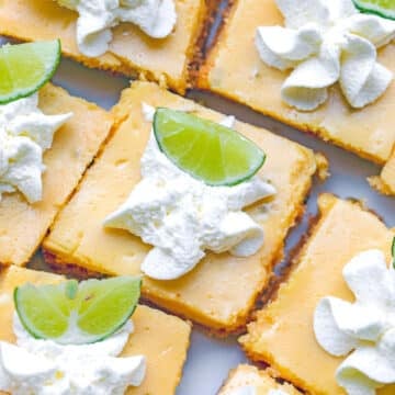 Overhead view of multiple key lime bars with whipped cream dollops and lime wedges.