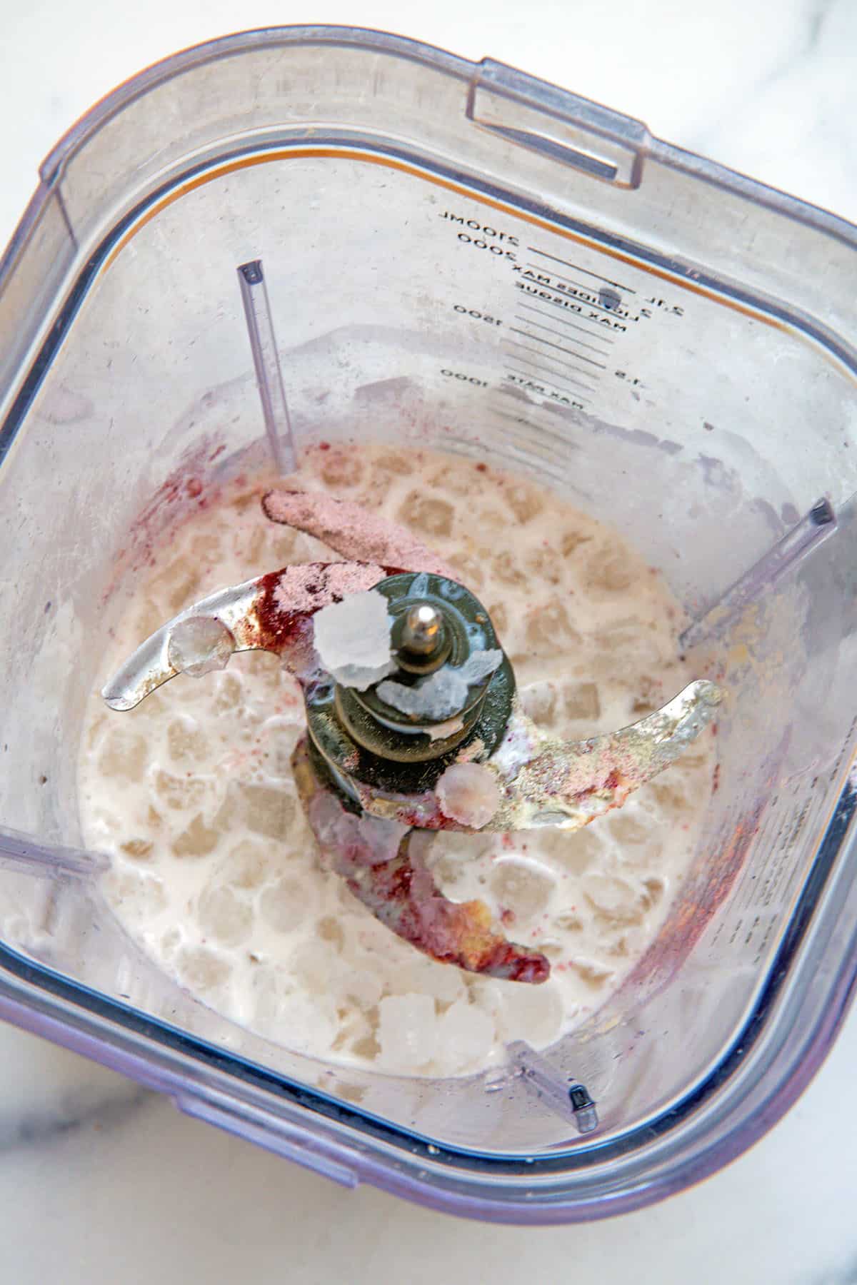 Overhead view of milk, xanthan gum, lavender powder, and vanilla syrup with ice in blender.