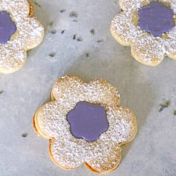 Closeup view of flower-shaped cookies with lavender icing in the middle and powdered sugar on top.