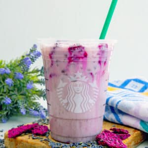 Head-on closeup view of a Lavender Oatmilk Chill with green straw in it and freeze-dried dragonfruit all around.