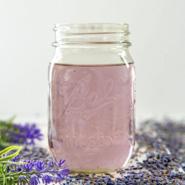 Closeup view of a mason jar of lavender syrup with dried flowers all around.