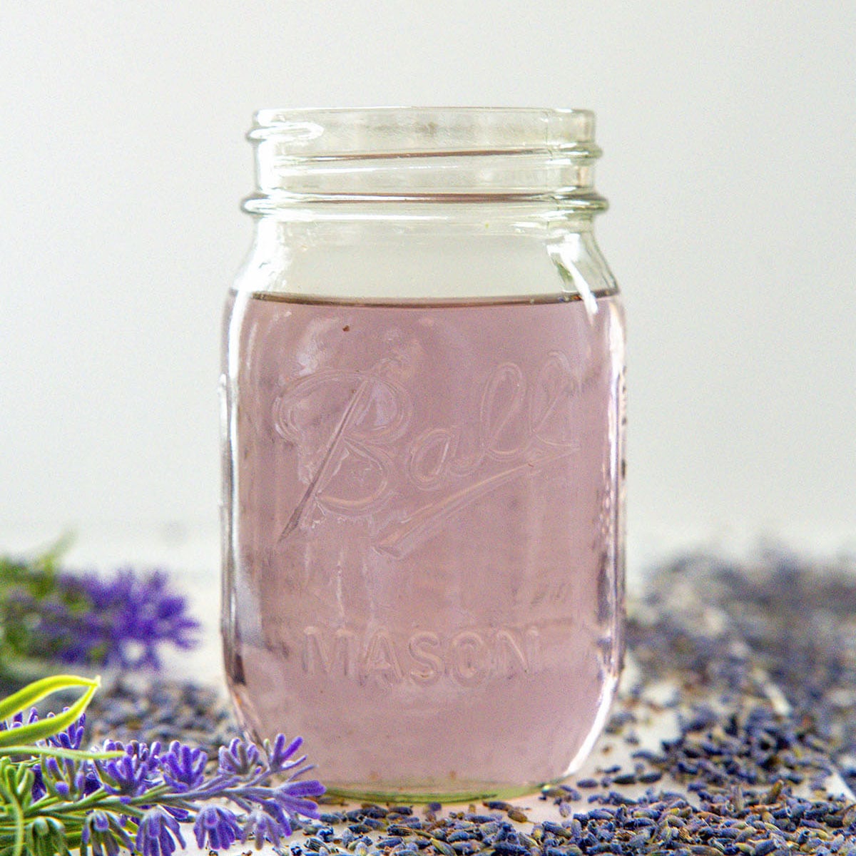 Closeup view of a mason jar of lavender syrup with dried flowers all around.