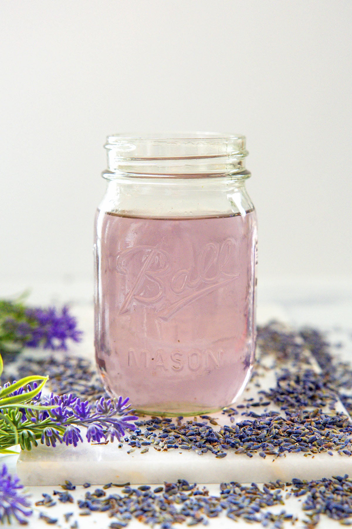 Head-on view of a mason jar filled with lavender simple syrup with lavender all around.