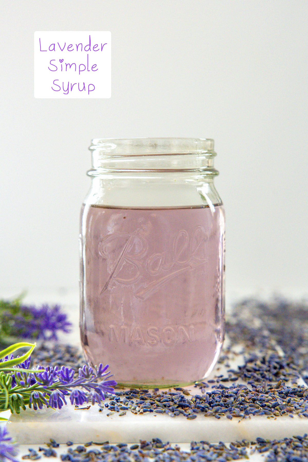 Head-on view of a mason jar filled with lavender simple syrup with lavender all around and recipe title at top.